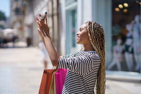 Young black woman photographing something in a shopping street with her smartphone