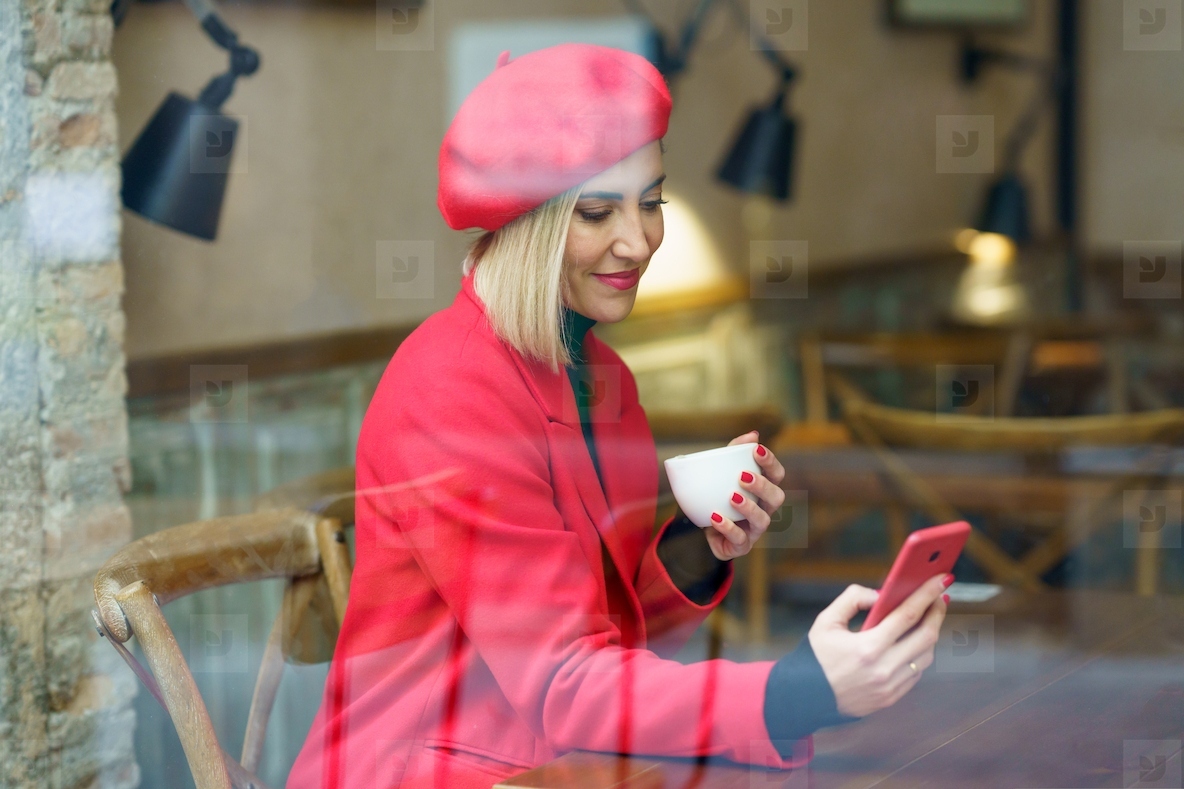 Woman drinking a cup of coffee in a coffee shop  while consulting her smartphone