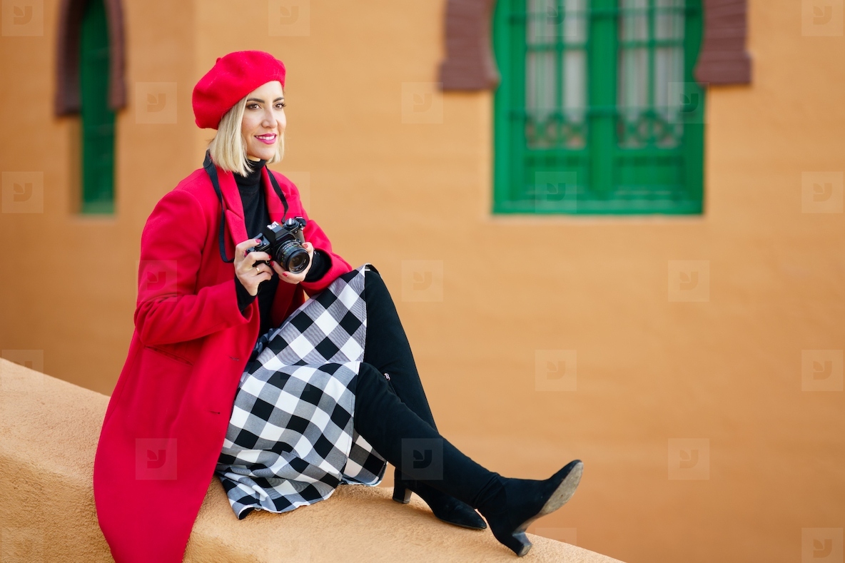 Woman wearing red winter clothes  taking pictures with an SLR camera sitting on a city wall