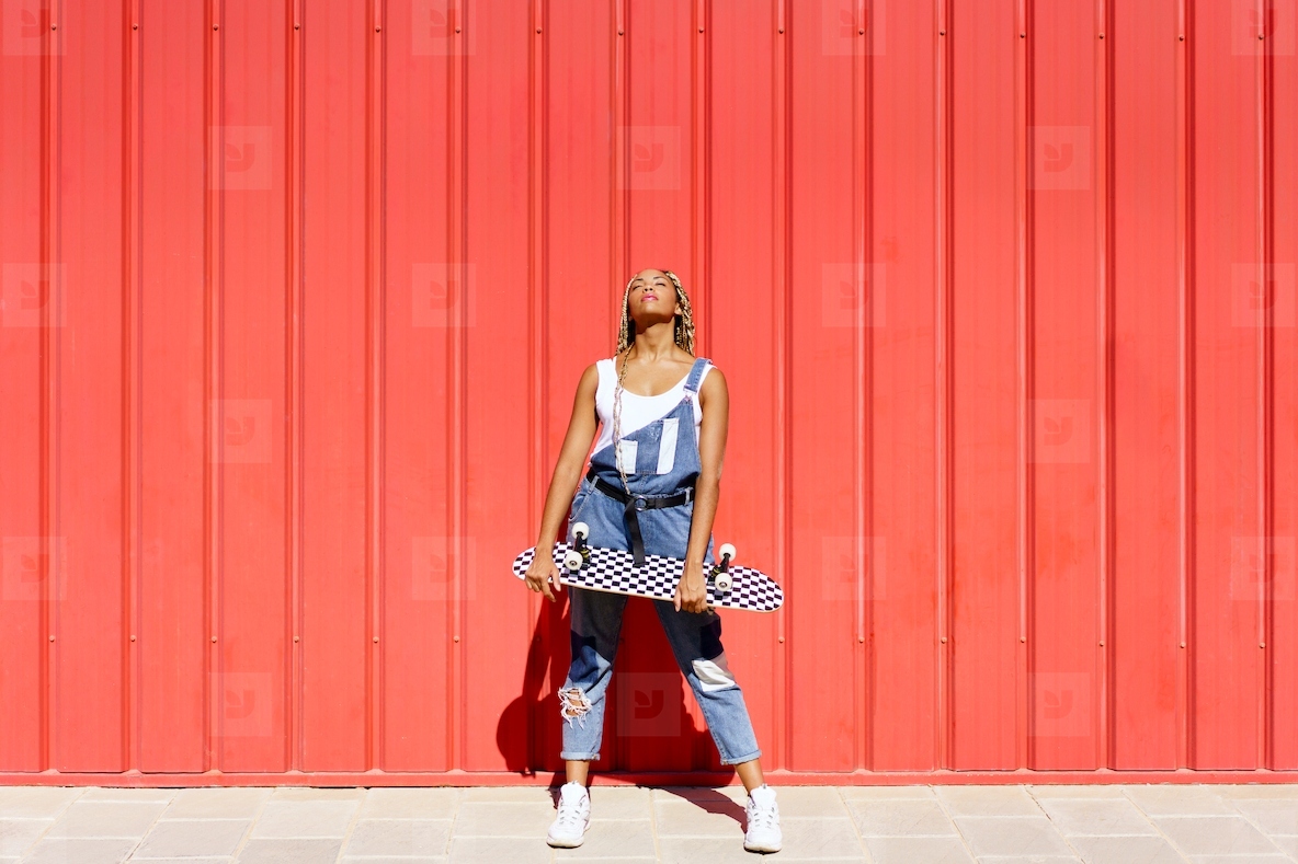Black girl dressed casual  wtih a skateboard on red urban wall background