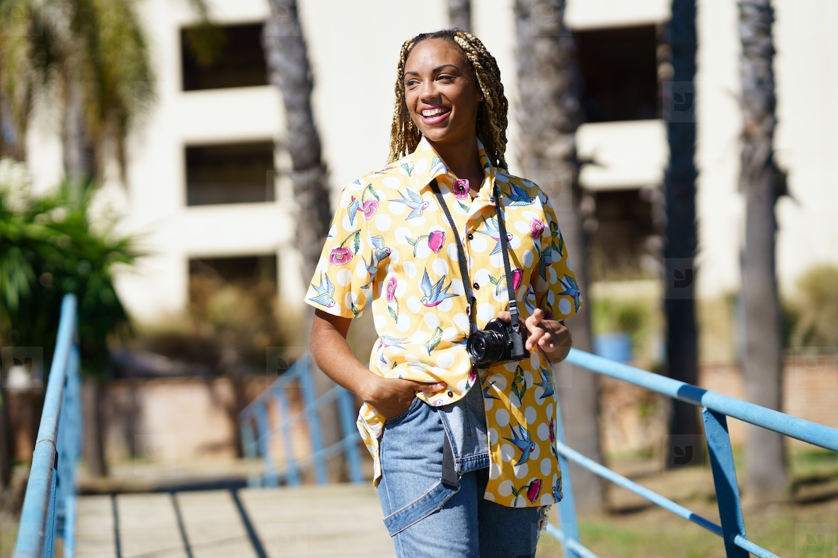 Happy black female combed with colorful braids walking with a camera on vacation