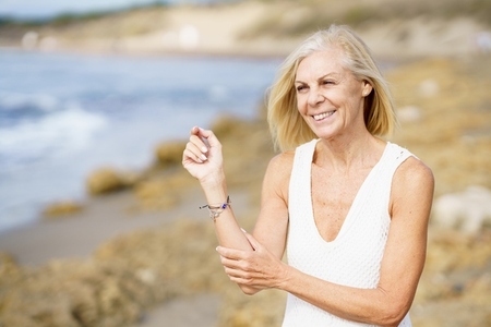 Smiling mature woman walking on the beach  Elderly female standing at a seaside location