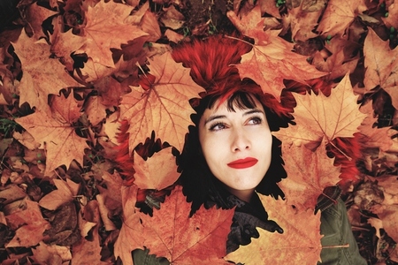 Young woman lying down in the floor full of autumn leaves