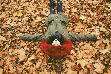 Young woman lying down in the floor full of autumn leaves