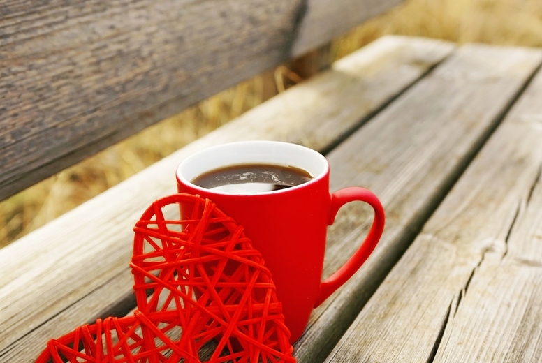 Red mug with coffee in a wooden bench outdoors in the morning