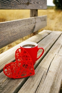 Red mug with coffee in a wooden bench outdoors in the morning