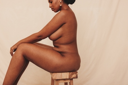 Unclothed woman sitting sideways in a studio