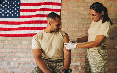 Female medic applying a band aid to a soldiers arm after vaccination