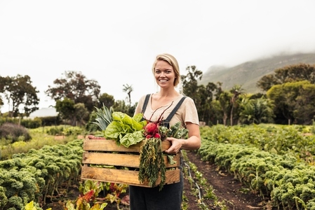 Smiling female farmer holding a box with fresh produce