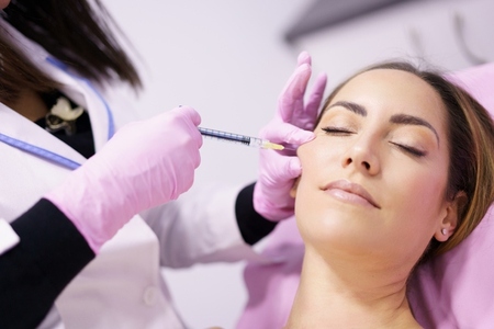 Doctor injecting hyaluronic acid into the cheekbones of a woman as a facial rejuvenation treatment