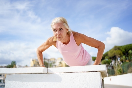 Mature woman working strength training push ups against sky with copyspace