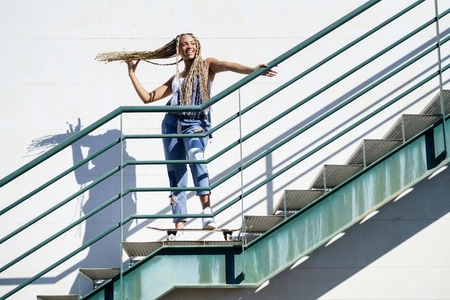 Black woman on an urban staircase  holding her coloured braids  Typical African hairstyle