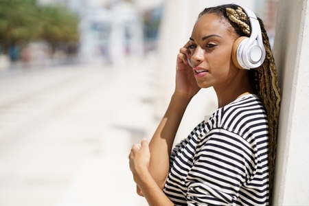 Young black woman listening to music with wireless headphones outdoors