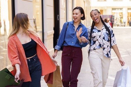 Cheerful young diverse ladies having fun on street after shopping