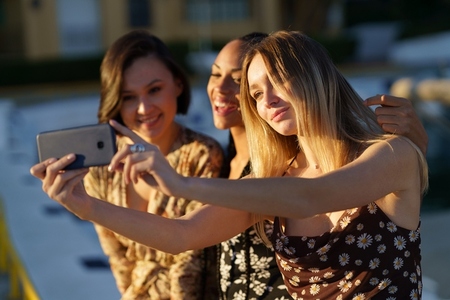 Charming diverse girlfriends taking selfie on smartphone