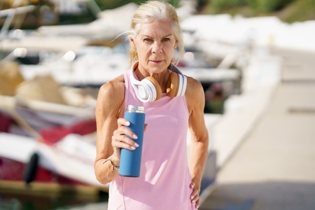 Senior woman in fitness clothing drinking water from a metal fitness bottle outdoors