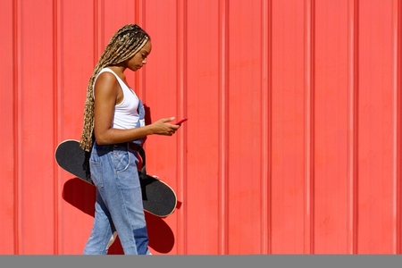 Black girl walking on an urban red background while consulting her smartphone