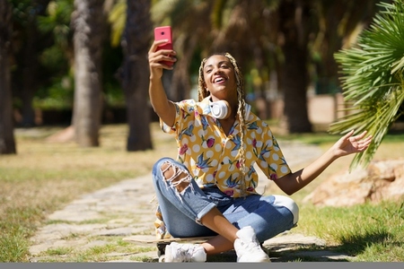 African girl with braided hair taking a selfie with a smartphone sitting on her skateboard