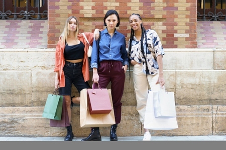 Stylish young diverse female friends standing on street after shopping