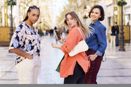 Trendy young multiracial female millennials looking at camera standing on city street