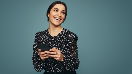 Cheerful young woman holding a mobile phone in a studio