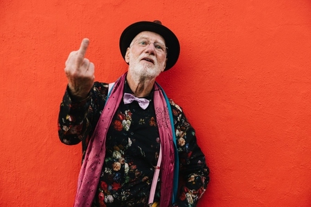 Mature man showing his middle finger against a red background