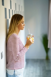 Pensive woman drinking a glass of natural orange juice at home