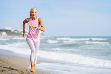 Older female doing sport to keep fit  Mature woman running along the shore of the beach