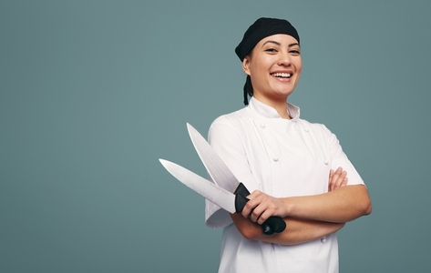 Cheerful culinary chef smiling while holding two knives