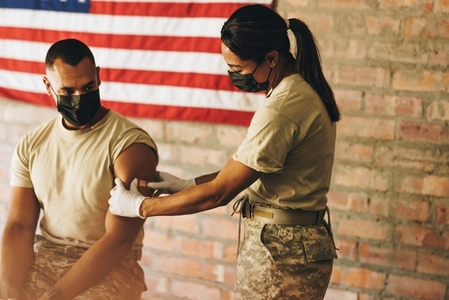Nurse applying a band aid to a soldiers arm after vaccination