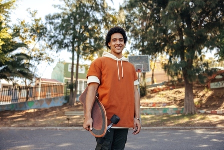 Cheerful skateboarder holding his skateboard in an urban park
