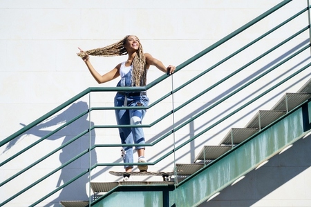 Black girl on an urban staircase  holding her coloured braids  Typical African hairstyle