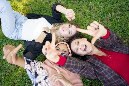 Cheerful ladies gesturing camera while lying on grass