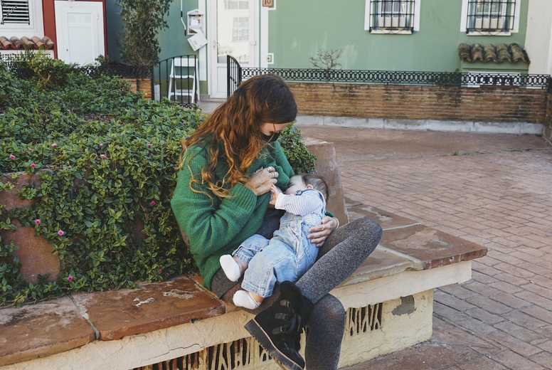 Young woman breastfeeding her baby outdoors in a sunny day