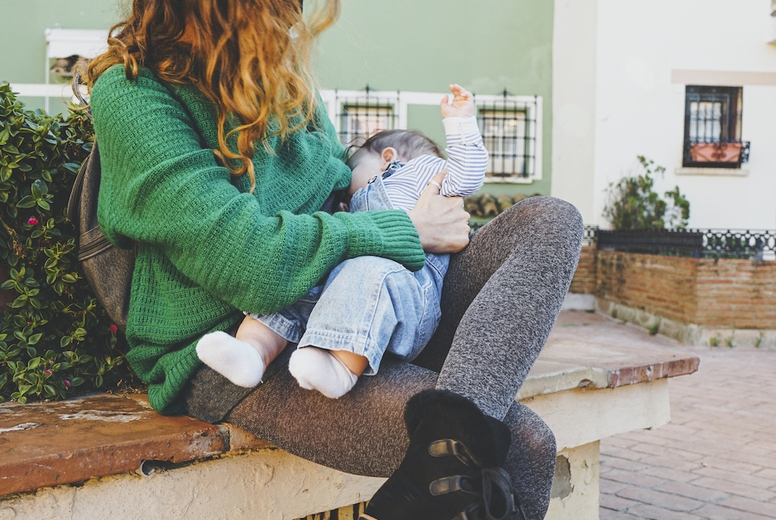 Young woman breastfeeding her baby outdoors in a sunny day