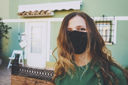Young woman wearing a black face mask against an urban green wal