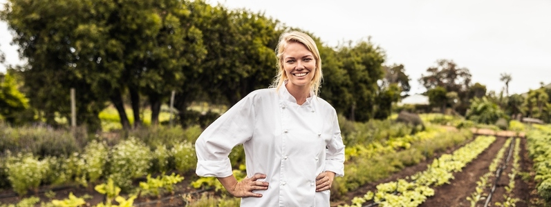 Cheerful young chef smiling at the camera on a farm