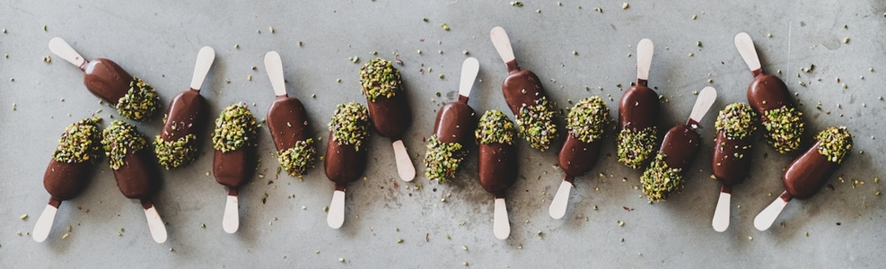 Chocolate glazed ice cream pops over grey background  wide composition