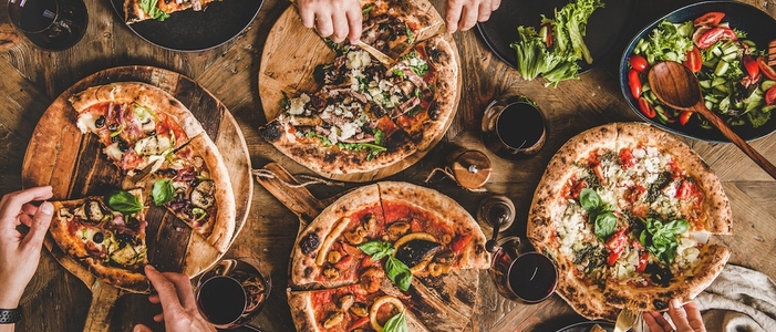 People eating various pizzas and drinking red wine  wide composition
