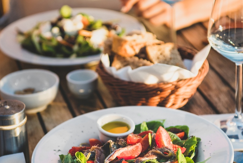 Young woman eating salad and drinking wine in italian cafe