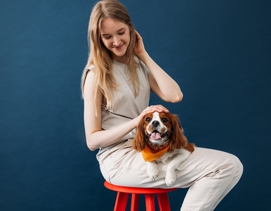 Young woman in casuals sitting on a red chair in studio with her little dog