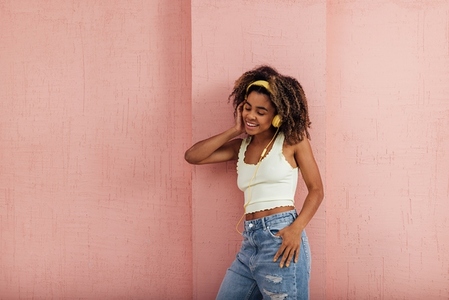Young stylish woman wearing yellow headphones leaning a pink wall