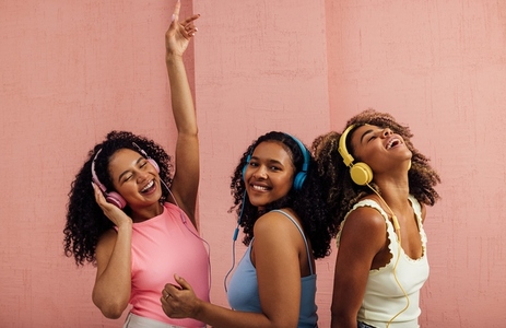 Three young women with curly hair wearing headphones and dancing