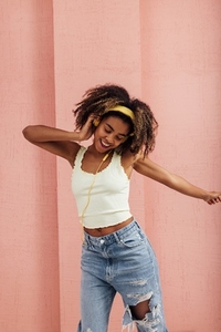 Young woman wearing yellow headphones at pink wall and dancing
