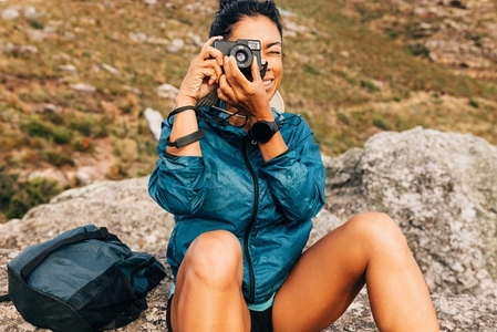 Woman hiker filming scenery while taking a break on a hill during climbing