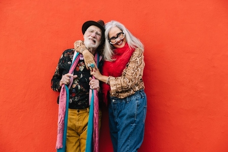 Happy elderly couple smiling cheerfully against a red wall
