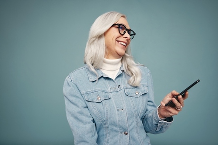 Cheerful grey haired woman holding a amsrtphone in a studio