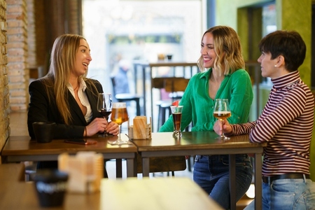 Cheerful girlfriends gathering around table in bar