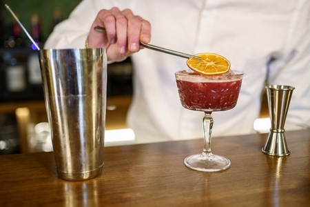 Crop barman garnishing cocktail with citrus slice