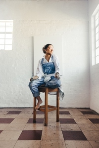 Contemplative female artist sitting on a chair in her studio
